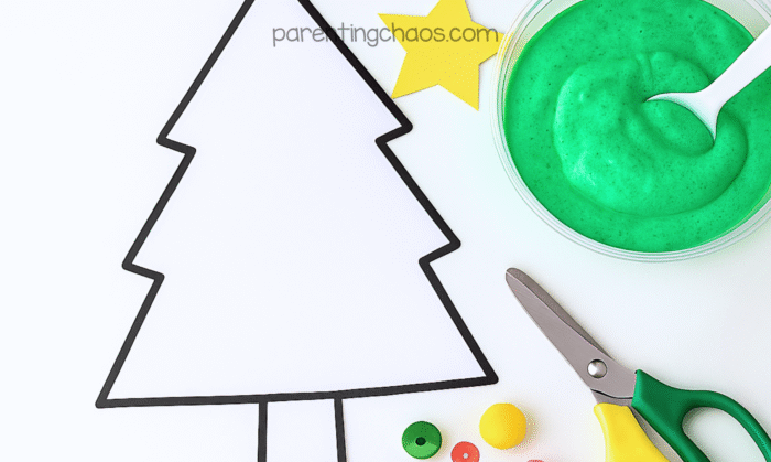Christmas tree outline on white paper surrounded by craft supplies and a bowl of green puffy paint, ready for painting.