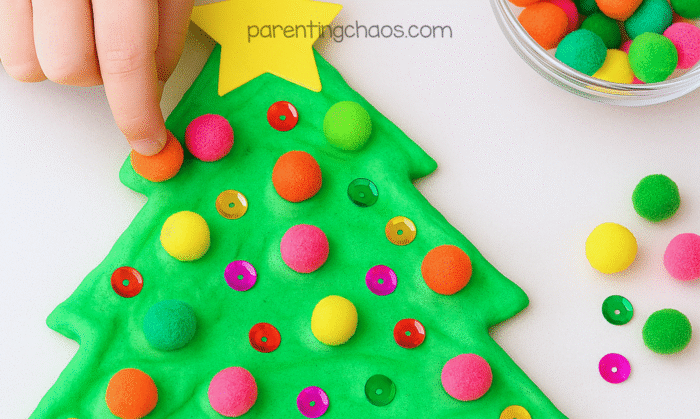 Child decorating the puffy paint Christmas tree with colorful pom poms and sequins to look like ornaments.