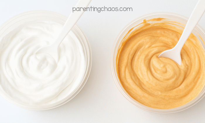 One bowl of white puffy paint beside another mixed into pumpkin-colored puffy paint with spoons in each.