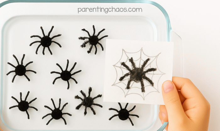 Child holding up paper showing a spider caught inside the web drawing after pressing it into the floating spider experiment.