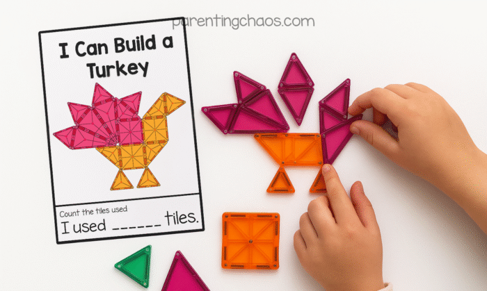 Close-up of a child’s hands building a turkey shape with magnetic tiles beside an “I Can Build a Turkey” task card. The card shows a completed turkey design in orange and pink tiles with space to record how many tiles were used.