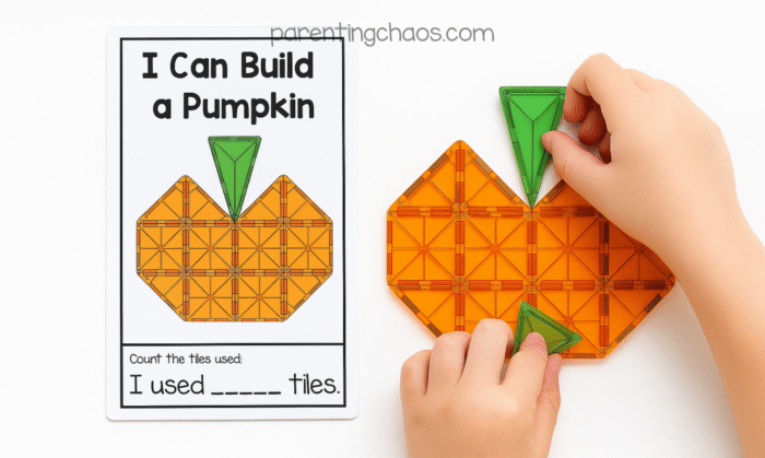 Close-up of a child completing an “I Can Build a Pumpkin” task card activity. The child’s hands place green triangular magnetic tiles to finish the pumpkin stem beside the printed card that shows the completed pumpkin shape.