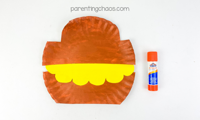 Treasure chest paper plate craft assembly showing brown paper plate pieces and yellow coin layer with glue stick.